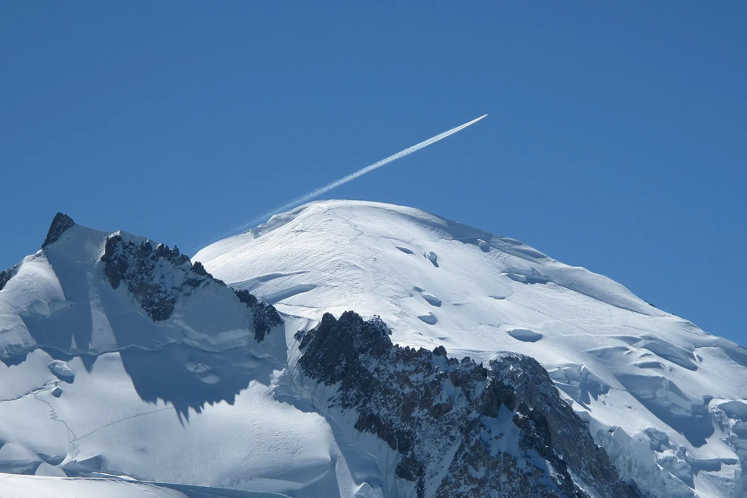 An airliner and its contrail high above the snow-covered summit of Mont Blanc.