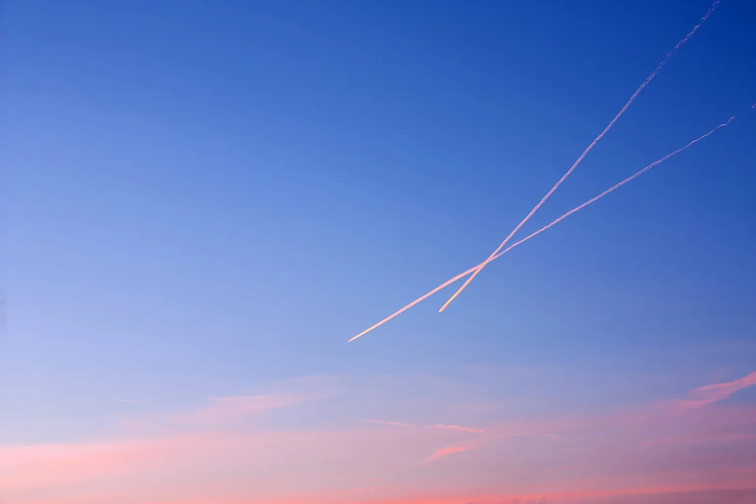 Two contrails crossing high in a clear sky at sunset.