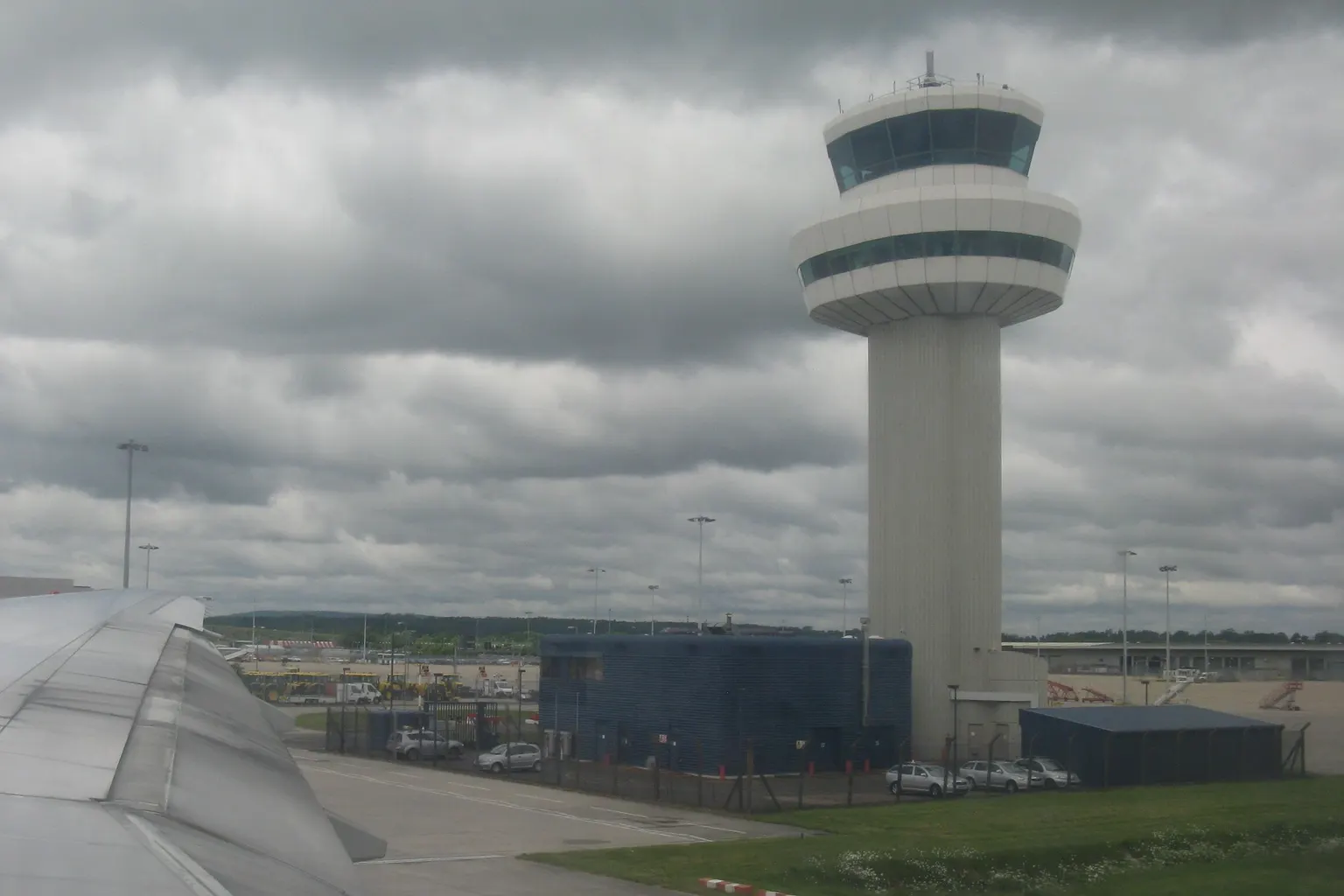 The air traffic control tower at Gatwick Airport under grey cloud, seen past an aircraft wing.
