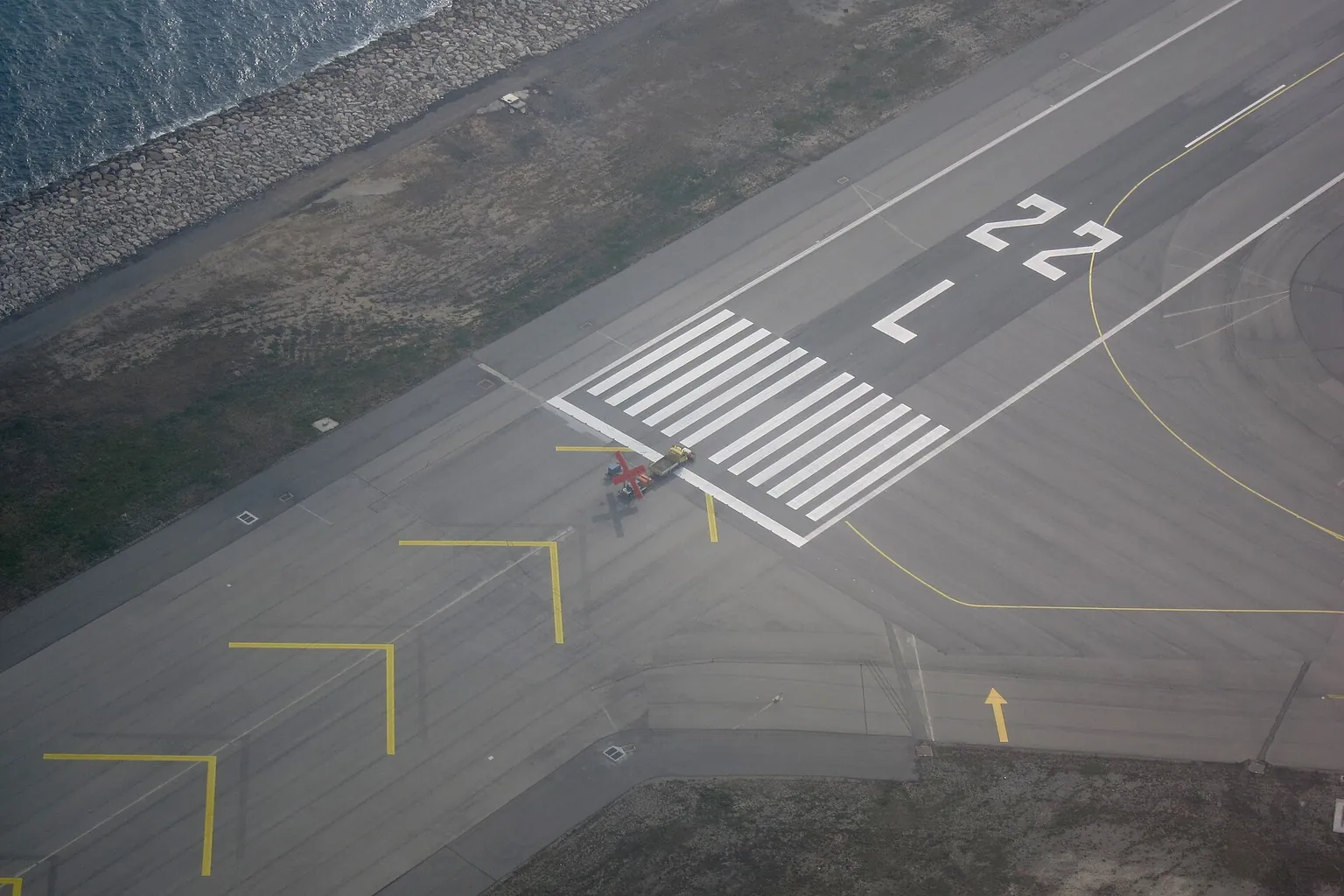 An aerial view of the end of runway 22L, with its number and white threshold stripes.
