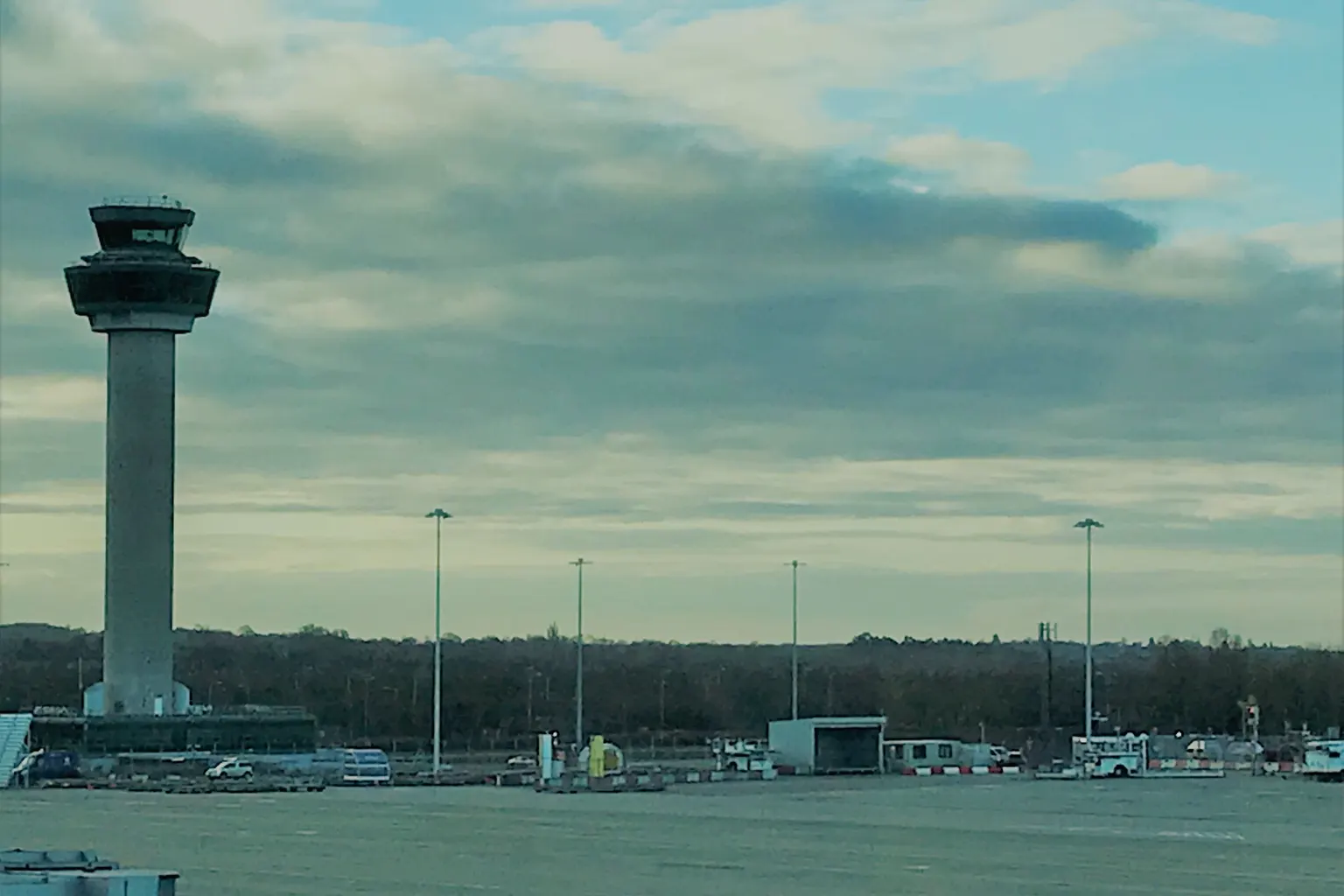 The control tower at London Stansted Airport across an empty apron, under a cloudy sky.