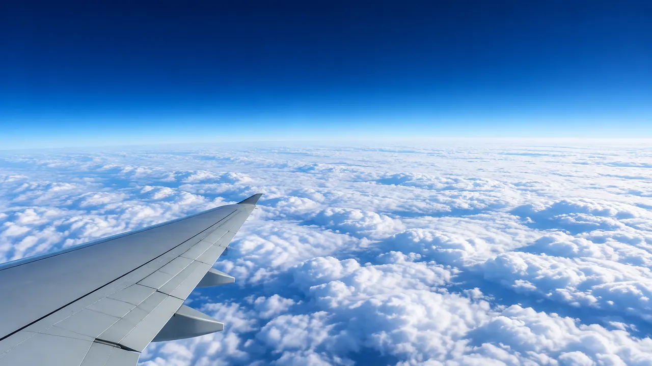 A plain wingtip far above a flat sea of white cloud, the sky dark blue at a softly curving horizon.