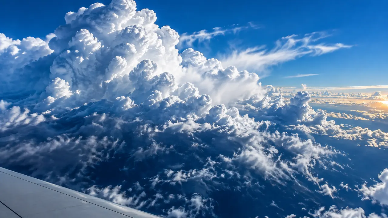 Towering cumulus clouds boiling upward beside a plain wingtip at cruising height.