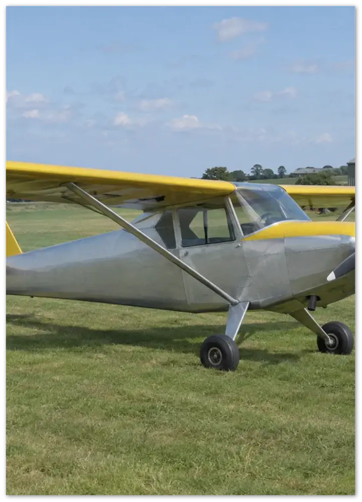 Render of an unframed portrait paper poster: a silver light aircraft with yellow wings parked on grass, printed as photographed.