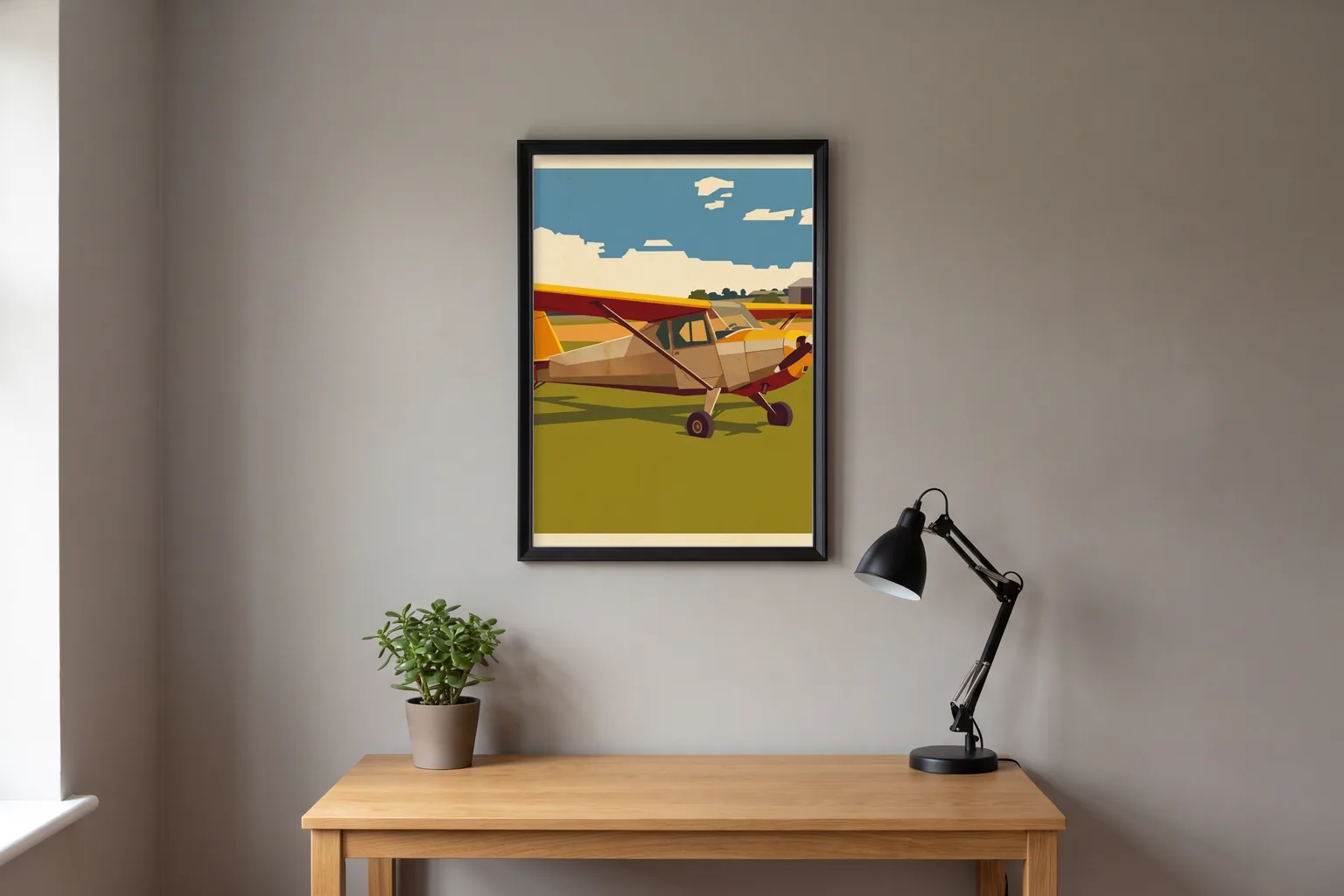 Illustrated mockup: a vintage-poster style print of a red and yellow light aircraft in a slim black frame above an oak desk with a lamp and a plant.